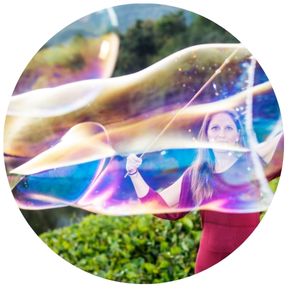 Picture of woman with two sticks creating a giant bubble.