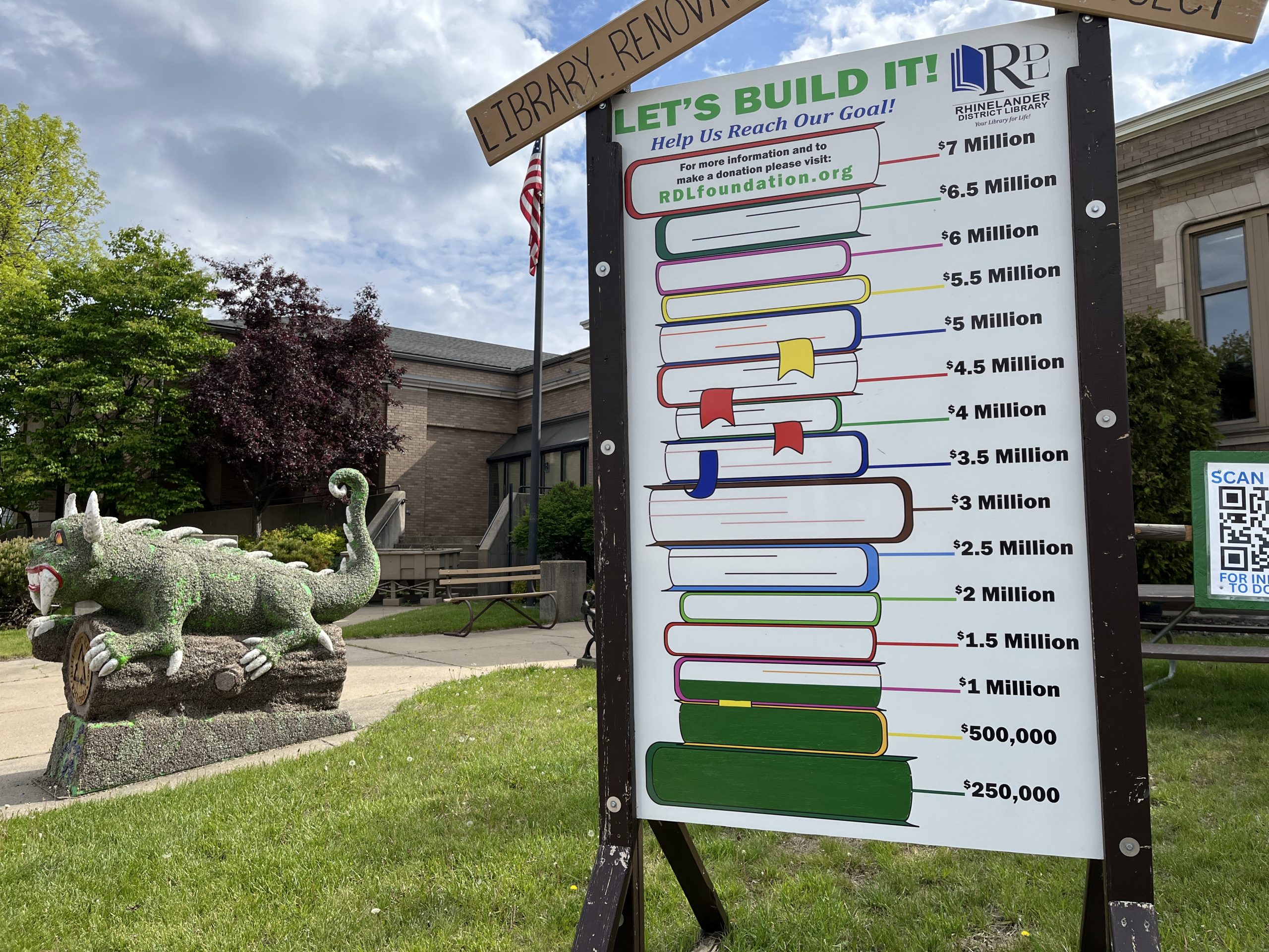 Hodag on cement next to a sign with stacked books and a sign with green marking a million dollars