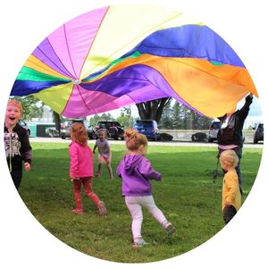 Kids playing under a colorful parachute on a park lawn