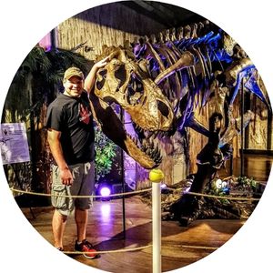 Picture of a man in a baseball cap next to a large dinosaur fossil